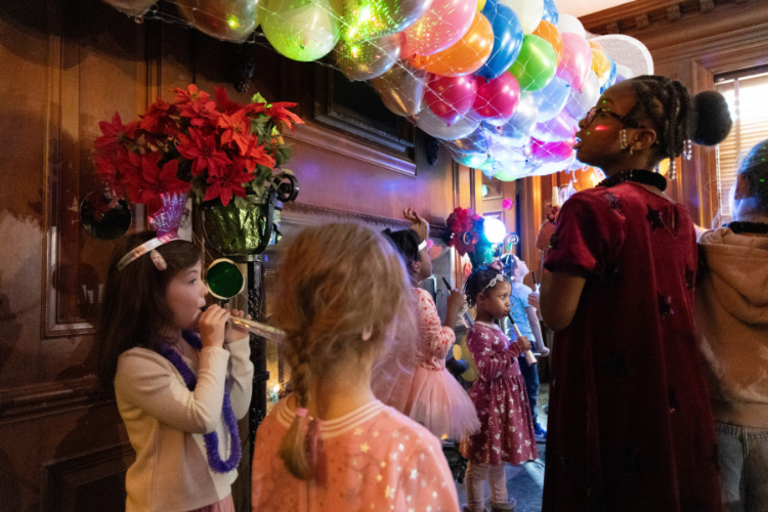 Children celebrate with balloons and noisemakers, photograph.